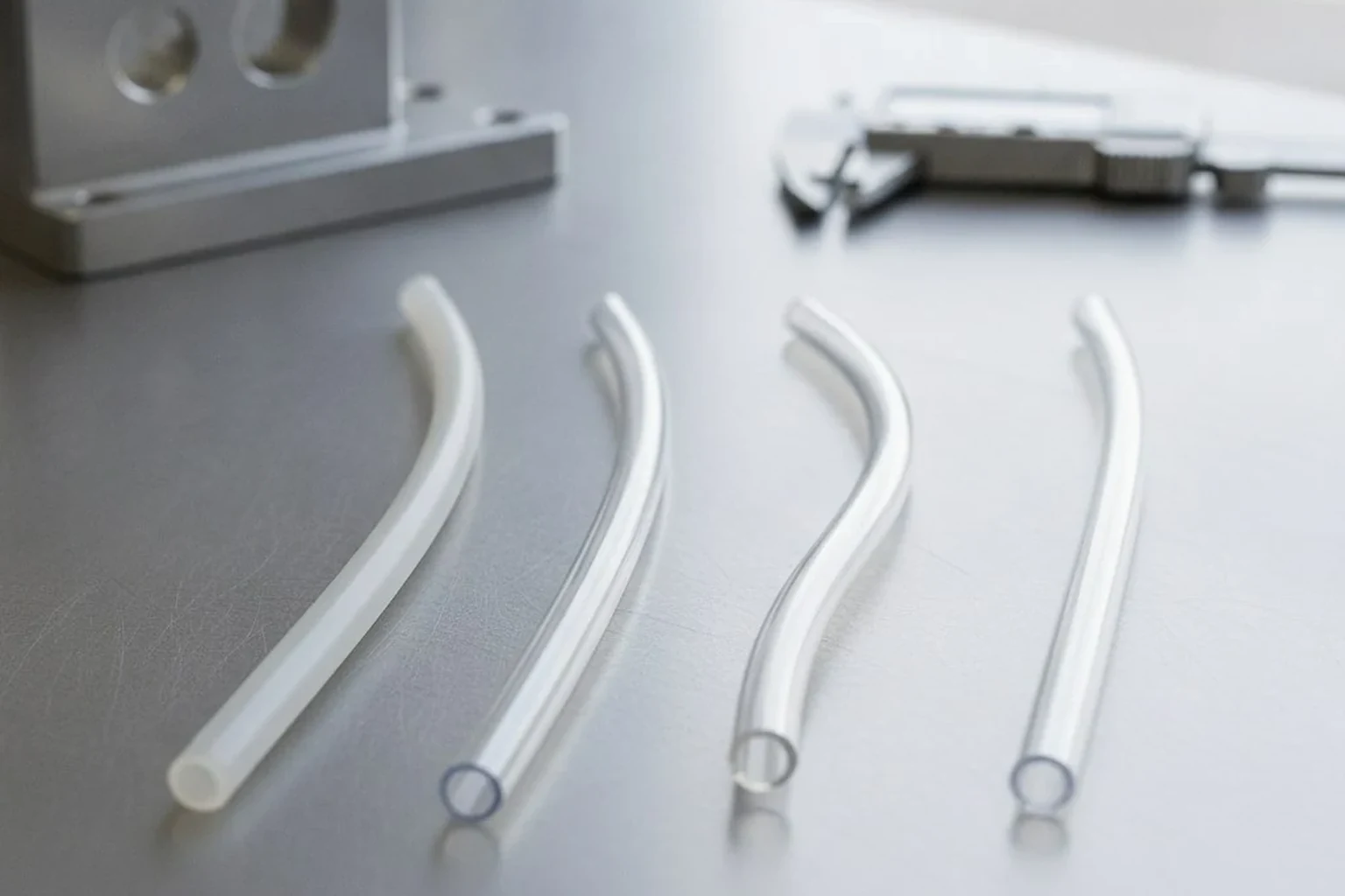 Photorealistic B2B industrial website image for PTFE vs PFA vs FEP vs ETFE tubing selection guide, four fluoropolymer tubing samples on a clean engineering workbench